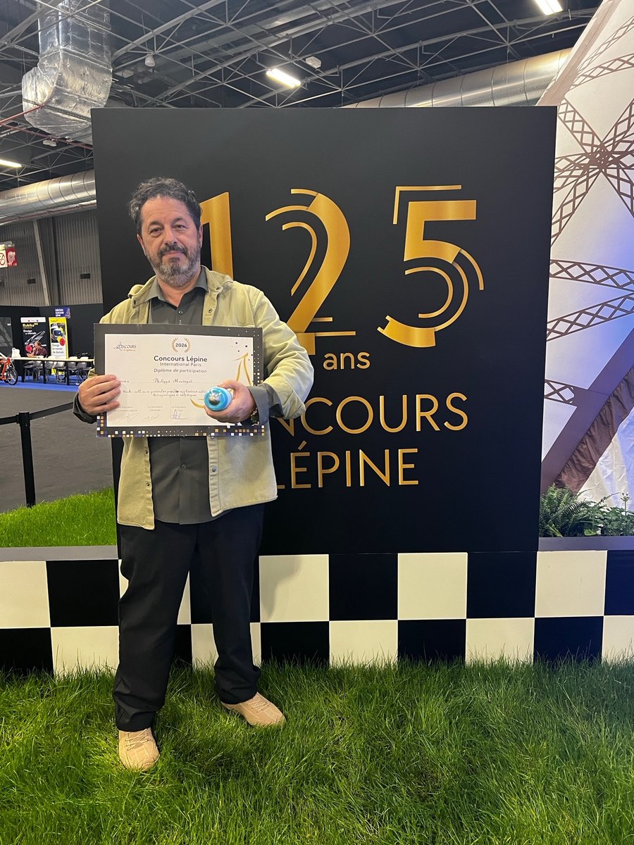 Philippe Montégut tenant son diplôme devant le mur des 125 ans du Concours Lépine.